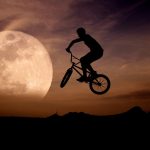 Ciclista con su bicicleta saltando con la luna llena de fondo