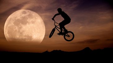 Ciclista con su bicicleta saltando con la luna llena de fondo